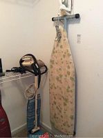 Photo showing the ironing board, Rowenta iron mounted on the wall, Shark iron and Hoover vacuum in the corner.