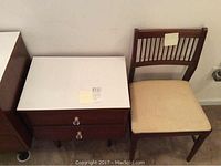 Photo of 1950's style wood night stand with white Formica-like top and adjacent wooden slat-back chair with cream cushion.