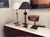 Three lamps on a dresser, showing the silver-tone table lamp, copper-tone table lamp, and copper-tone desk lamp.