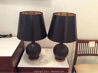 Pair of black mid-century style table lamps with spherical bases made of glass on wooden stands, black lampshades with gold inner lining, approximately 22 inches tall each.