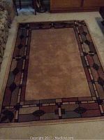 Full view of brown area rug showing central plain tan section and decorative patterned border with leaves and geometric shapes.