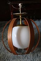 Side view of mid century modern hanging globe light fixture with curved teak wood slats surrounding white glass globe.