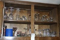 Cabinet shelf containing various stemware, snifters, patterned glasses and blue coasters.