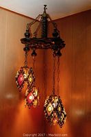 Full view of the hanging chandelier showing four colored glass caged lights suspended from dark wood frame with metal chains.