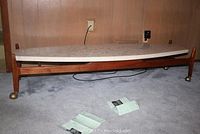 Full view of elongated surfboard-shaped coffee table showing white terrazzo top and teak wood base on carpeted floor