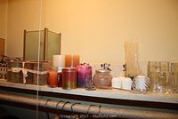 Wide view showing assortment of various candles in different colors and sizes along a shelf, alongside candleholders and decorative items.