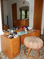 Full view of Heywood Wakefield vintage vanity table with large attached mirror and flower-style cushioned round stool, with personal items on top of the vanity.