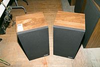 Pair of wooden cabinet speakers with black grill covers placed on a wooden floor.
