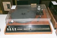 Front and top view of ADC Accutrac 4000 turntable with wood base and clear plastic dust cover closed, showing control buttons and tonearm.