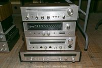 Stacked view of four vintage stereo receivers with wood sides and metal front panels. Top unit is Akai AA-1010, second is Sansui 221, third is Technics SA-202, bottom is Noresco 2670.