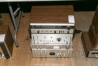 Photo showing stack of four vintage audio units including Fisher, Queon, Akai, and Kenwood electronics with wood side panels and metallic fronts.