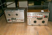 Two Telefunken reel to reel tape recorders placed side by side on the floor, showing front view with controls and meters visible.
