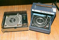 Overall view of two vintage manual turntables placed side by side on a wooden floor, showing the Electrohome Garrard and Zenith units.