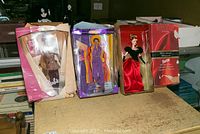 Three Barbie dolls in original packaging with visible damage to boxes on a wooden surface