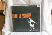 Photo showing the vinyl album 'Rattle and Hum' by U2 with black and orange cover art.