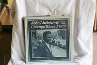 Stack of blues vinyl records showing John Littlejohn's Chicago Blues Stars album cover with a black and white portrait on city street.
