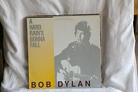 Vinyl record cover for A Hard Rain's Gonna Fall by Bob Dylan with image of Bob Dylan playing guitar.