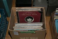 Cardboard box of vinyl records with Linda Ronstadt Greatest Hits album on top, showing some wear and creased corners