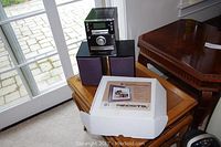 Symphony stereo system with two speakers and boxed Pandigital 8 inch digital photo frame on a wooden table near window.