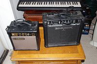 Yamaha GA-10 and Behringer GM108 guitar amplifiers on wooden table with keyboard in background