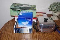 Overview of the lot showing the boxed chip and dip set, Oneida crystal box, chafing dish, and electric frypan on a table.