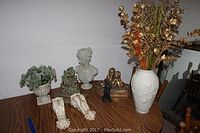 Overall view of Lenox vase with dried flowers, plaster bust of a woman, gold-painted plaster cherub sculpture, two tiebacks, and faux plant on table.