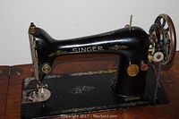 Close-up of black Singer sewing machine with gold decorative decals mounted in wooden top.