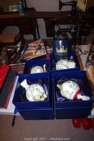 Four white floral themed musical ornaments in blue satin-lined boxes, displayed on table with Smithsonian Collection booklet included.