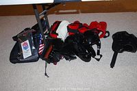 Photo showing a variety of martial arts training gear including gloves, helmets, pads, and a carrying bag arranged on the floor under a table.
