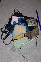 Lot showing several ladies purses stacked on carpet, displaying variety of styles and materials.
