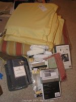 Overall view showing stacked light yellow fabric pieces, beige/red striped fabric underneath, and various packaged pillow shams and valances around them.