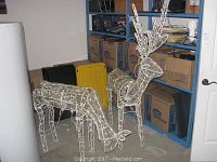 Front view of two wire-frame light-up reindeer decorations on floor with shelves and boxes in background.