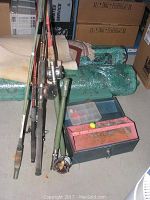 Fishing rods leaning against boxes with two green rod cases visible, several tackle boxes on floor