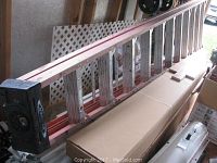 Side view of the Werner 12 ft aluminum extension ladder showing orange rails and black end caps with the ladder leaning indoors.