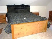 Full view of the bed with bedspread and pillows on carpeted floor, showing the wood paneled footboard and part of headboard