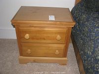 Full view of the wooden nightstand alongside a bed, showing the top surface and overall shape.