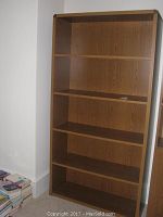 Front view of the tall wooden bookshelf showing all five shelves, natural wood finish, and rounded edges on top corners.