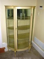 Vintage curved glass-front curio cabinet standing in a corner, showing closed door detail and legs.