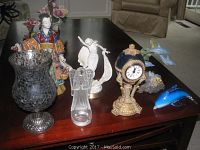 Wide view of assorted decorative items on table including glass vase, figurines, clock, and dolphin sculptures.