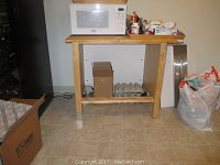 Wooden IKEA table in kitchen setting with microwave on top, showing table structure and size.