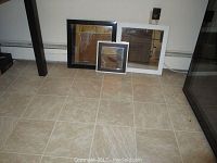 Three square framed mirrors on floor - one smaller silver-framed, two larger black and white framed.