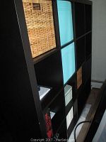 Angled front view of IKEA 16-cube storage unit showing blue fabric bins and woven wicker baskets in compartments.