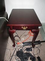Front and side view of the wooden side table showing a single drawer with a brass handle and curved legs.