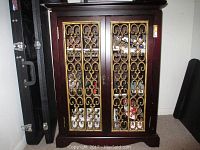 Front view of a rectangular wooden cabinet with two gold metal decorated doors. Cabinet appears used with one door off hinge and damaged metal scrollwork.