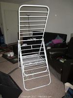 Full view of assembled white metal adjustable clothes dryer rack standing upright indoors on carpet near furniture.