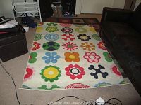 Top view of the IKEA Lusy Blom pattern area rug laid on floor showing colorful floral and abstract circular motifs on cream background.