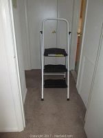 Stapleton three-step ladder shown fully upright in hallway, white frame and black steps visible.