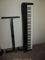 Casio PX-150 digital keyboard standing vertically beside the keyboard stand, power cord visible.