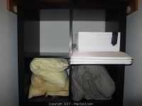 Front view of black-brown IKEA 4-cube storage unit with empty compartments. Some blankets and a box are visible, but not included.