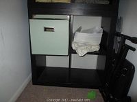 Front view of black IKEA 4-cube storage unit containing one green fabric cube bin and some white cloth inside an adjacent cube space. Unit is against a white wall, on carpet.